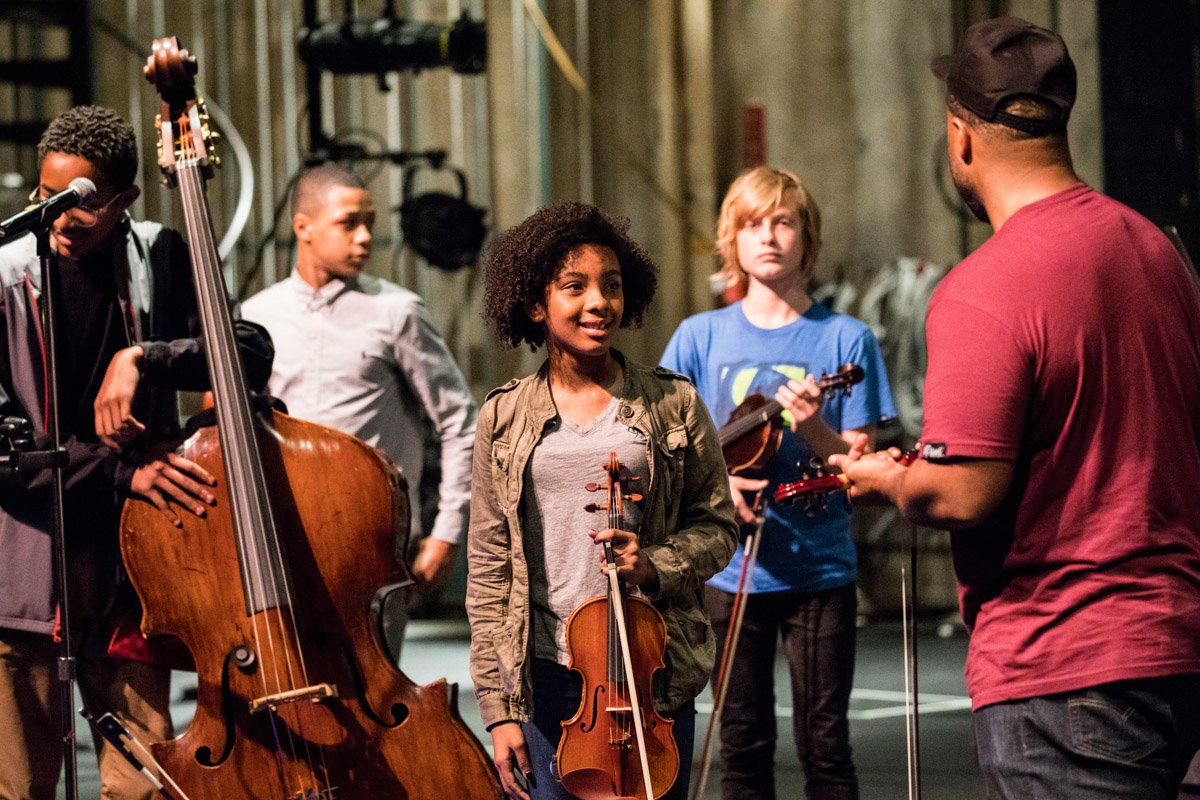 A group of students take instruction while practicing a performance.
