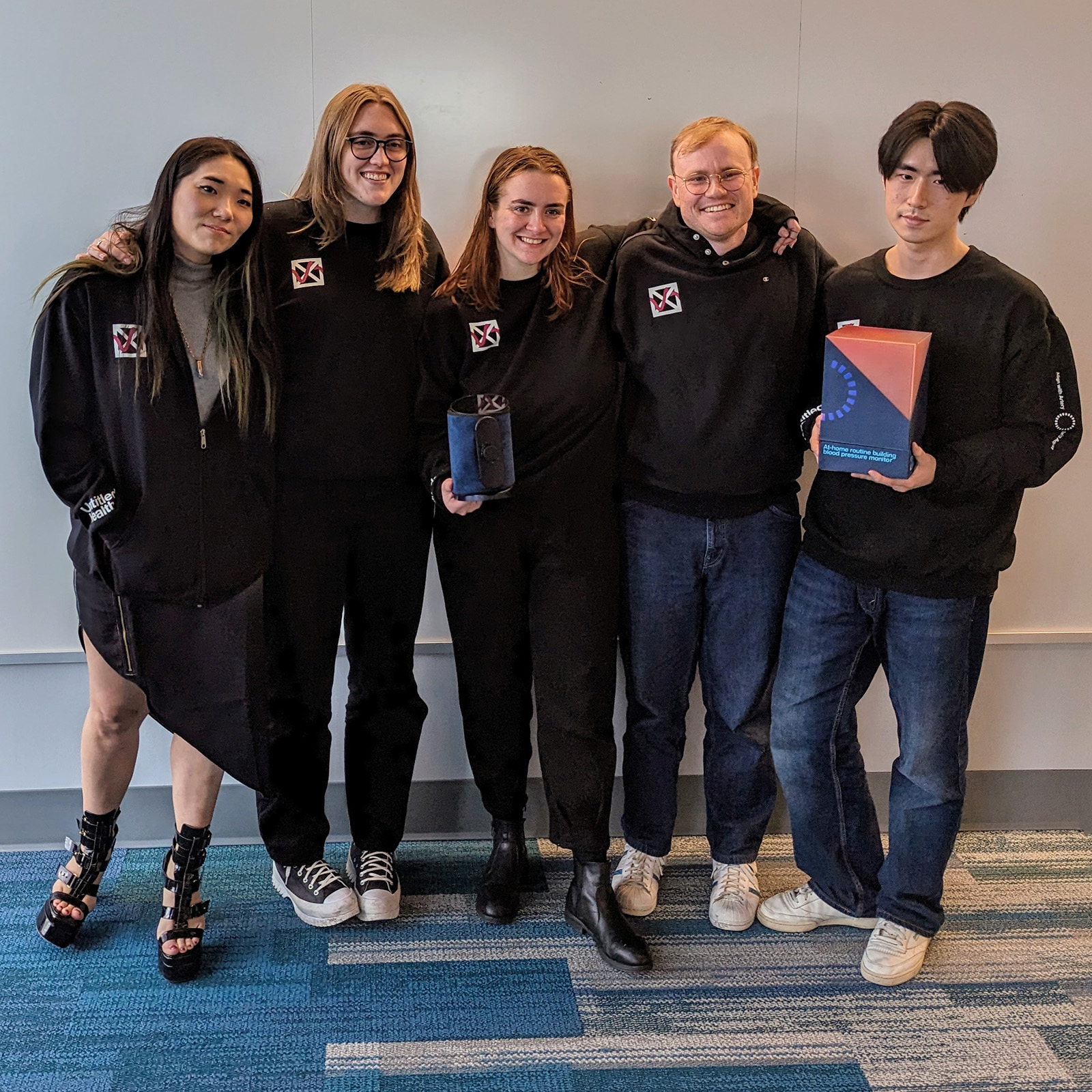 2. Group shot of the IPD thesis team after final presentations, posing with their final blood pressure cuff, charging dock, and packaging