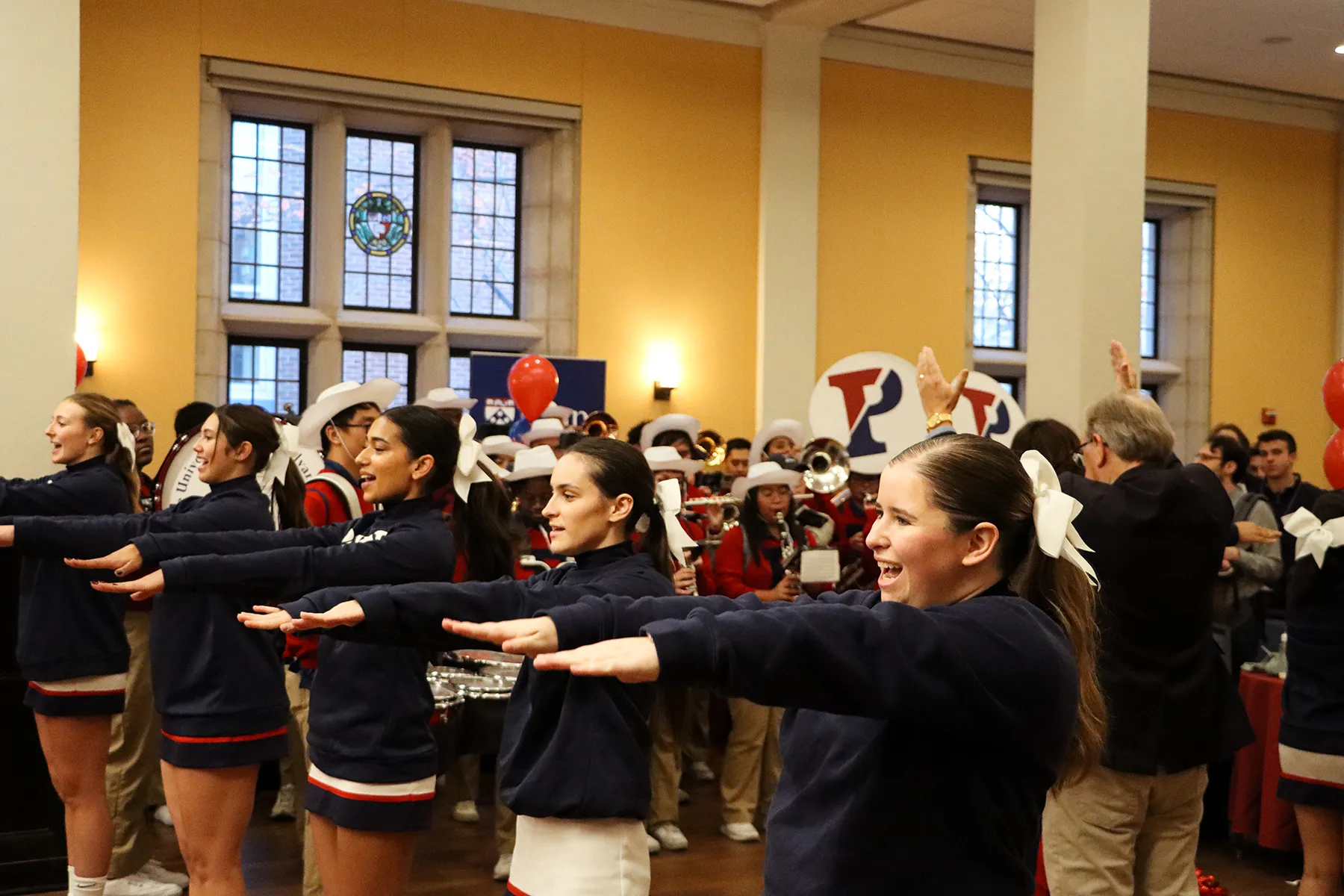University of Pennsylvania cheerleaders perform indoors alongside the pep band, with students and alumni gathered for a spirited homecoming event.