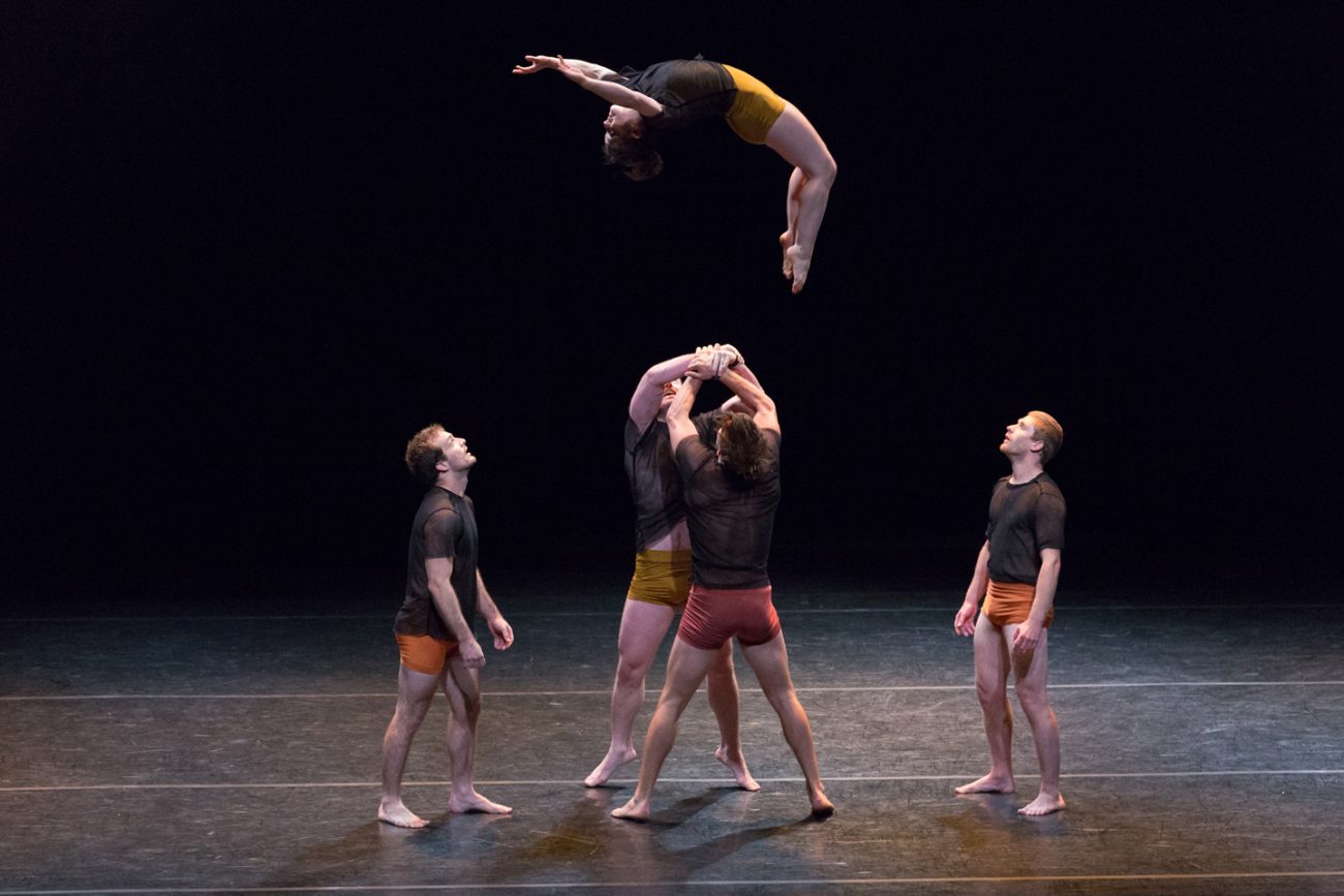 woman mid air doing back flip with spotters underneath her