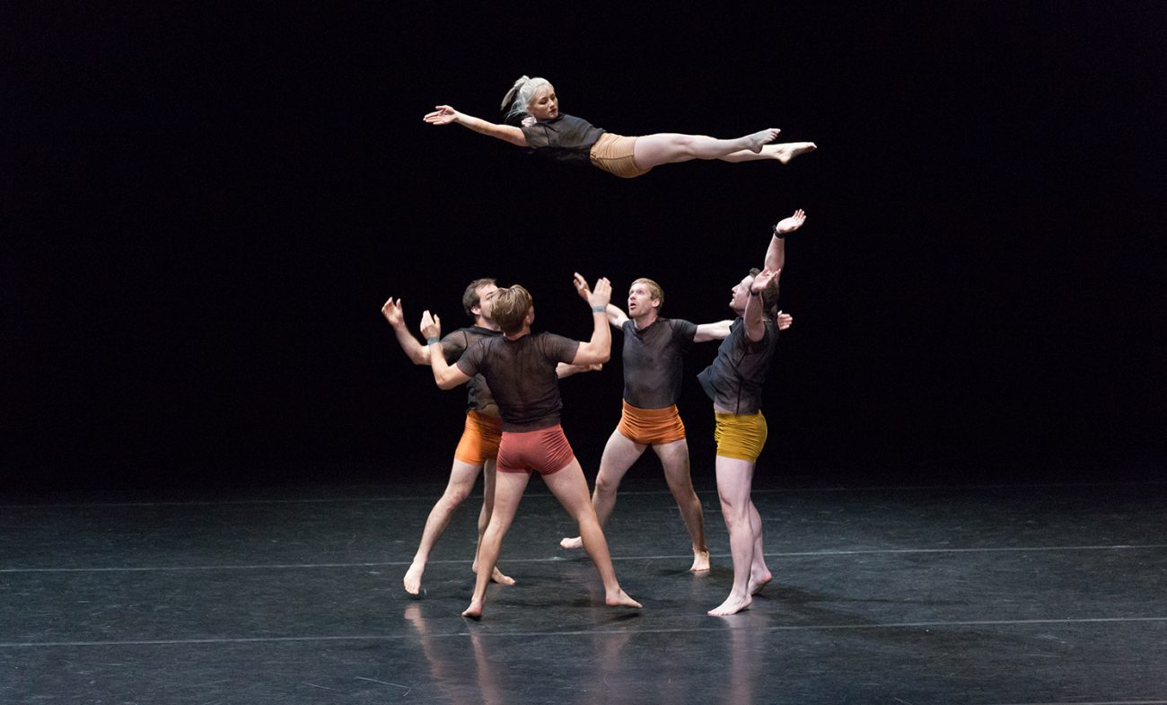 woman mid air doing a layout with spotters underneath her