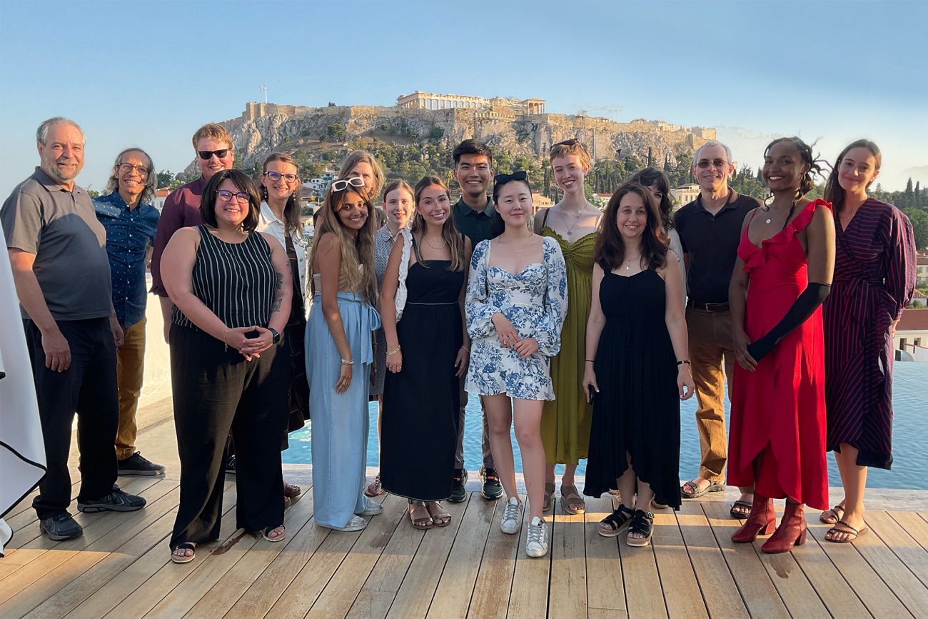A cohort of SNF Paideia Fellows stands together in front of the Acropolis in Athens, Greece.