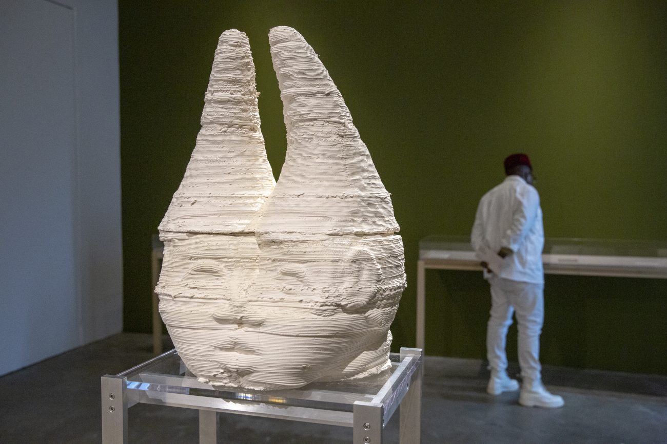 sculpture of two heads with cone shaped hats connected at the nose and mouth