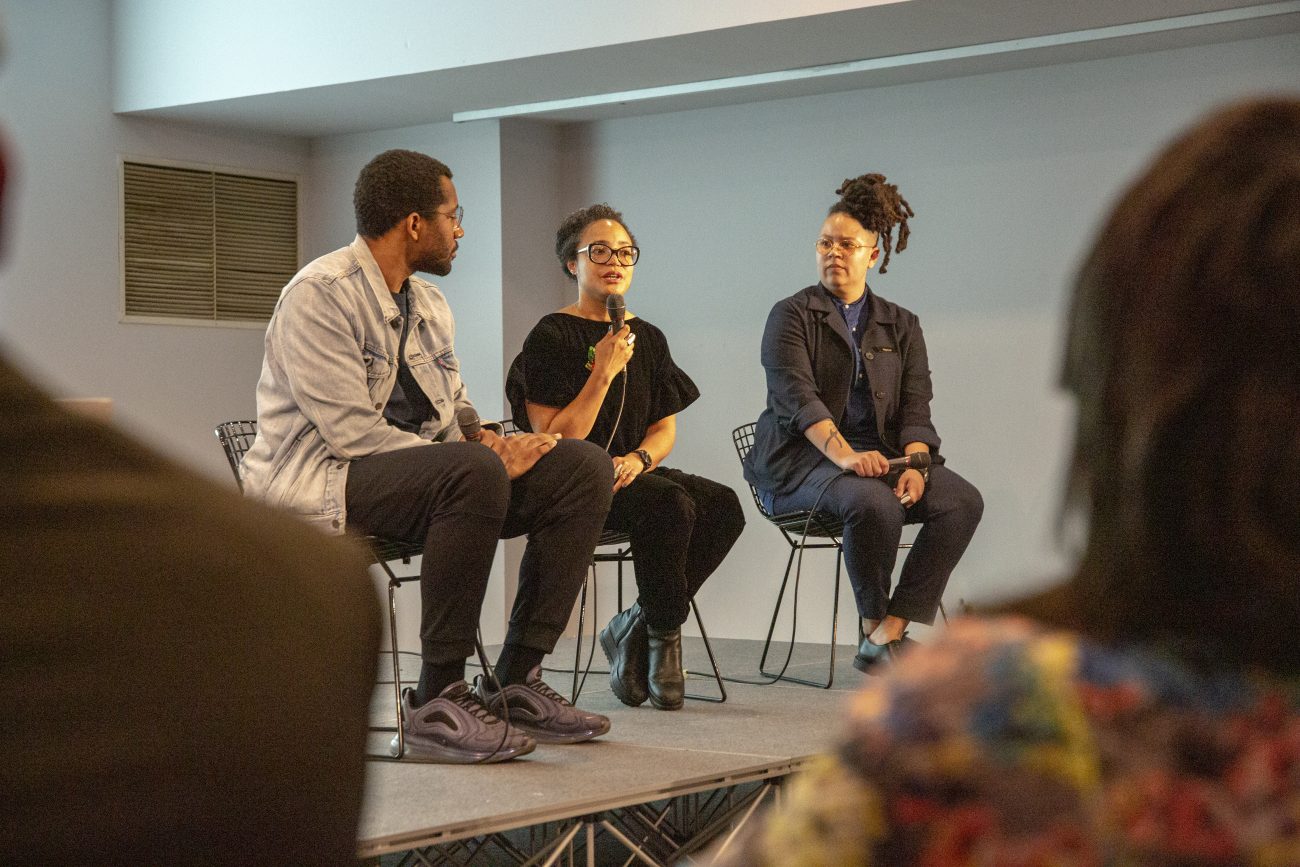 three people sitting on stage second individual is speaking into microphone