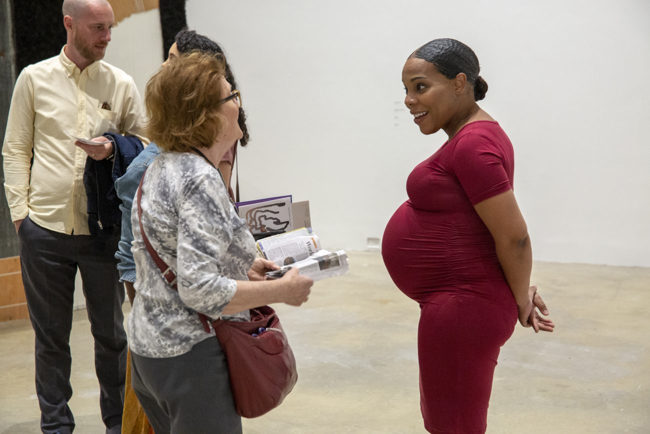 a pregnant worman in a red dress speaking with an older woman