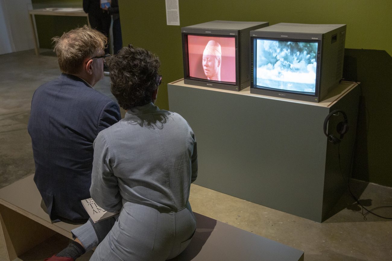 two people itting on a bench watching two box televisions