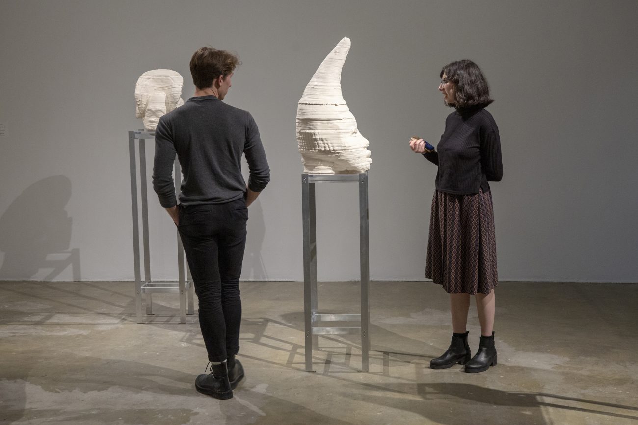two people looking at a sculpture of a face with a cone shaped head in a museum