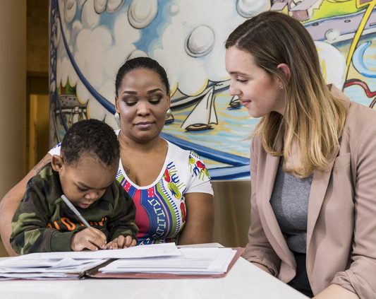A student learnes to write under the supervision of his mother and an instructor