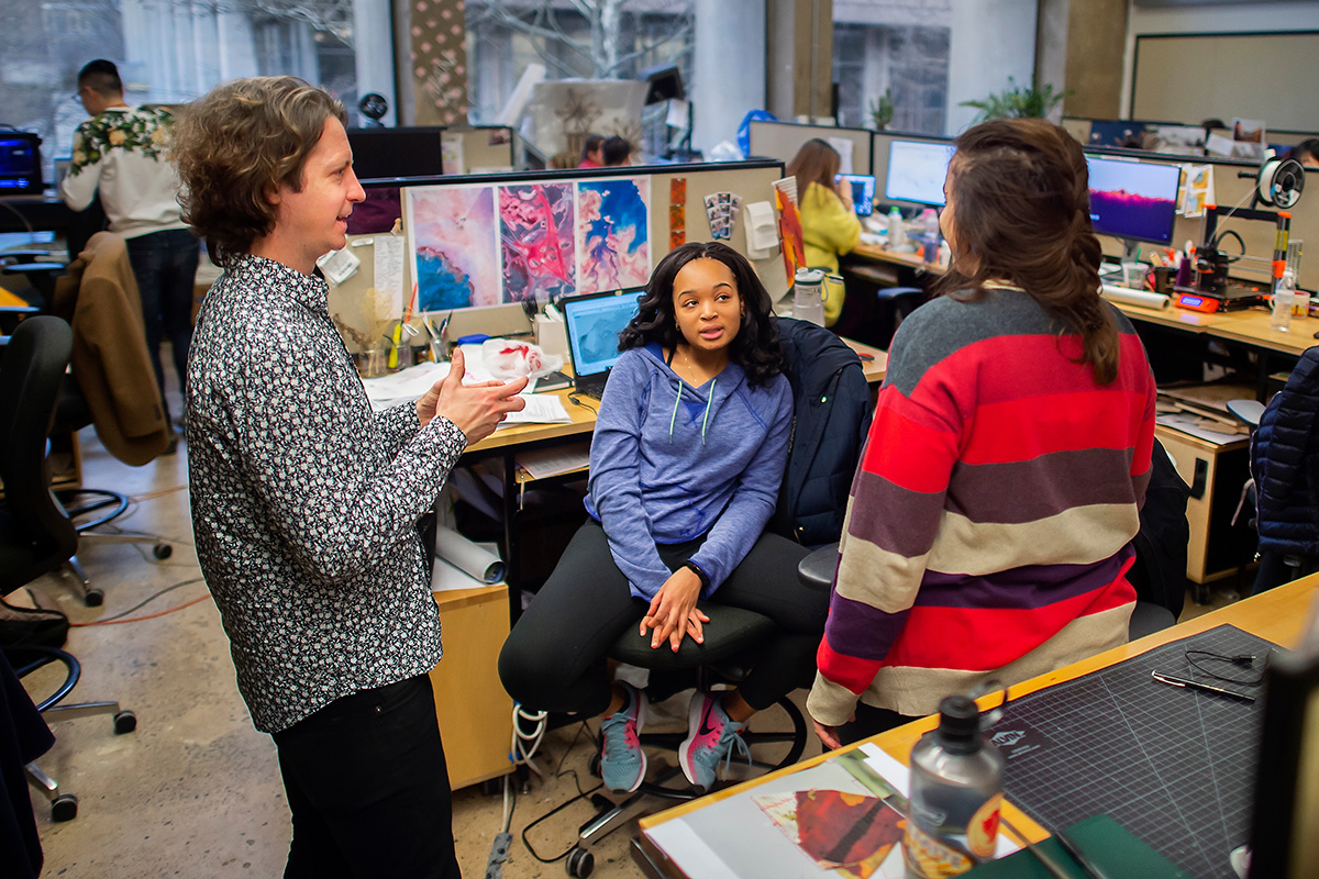 Three people carry on a discussion in a work room devoted to design