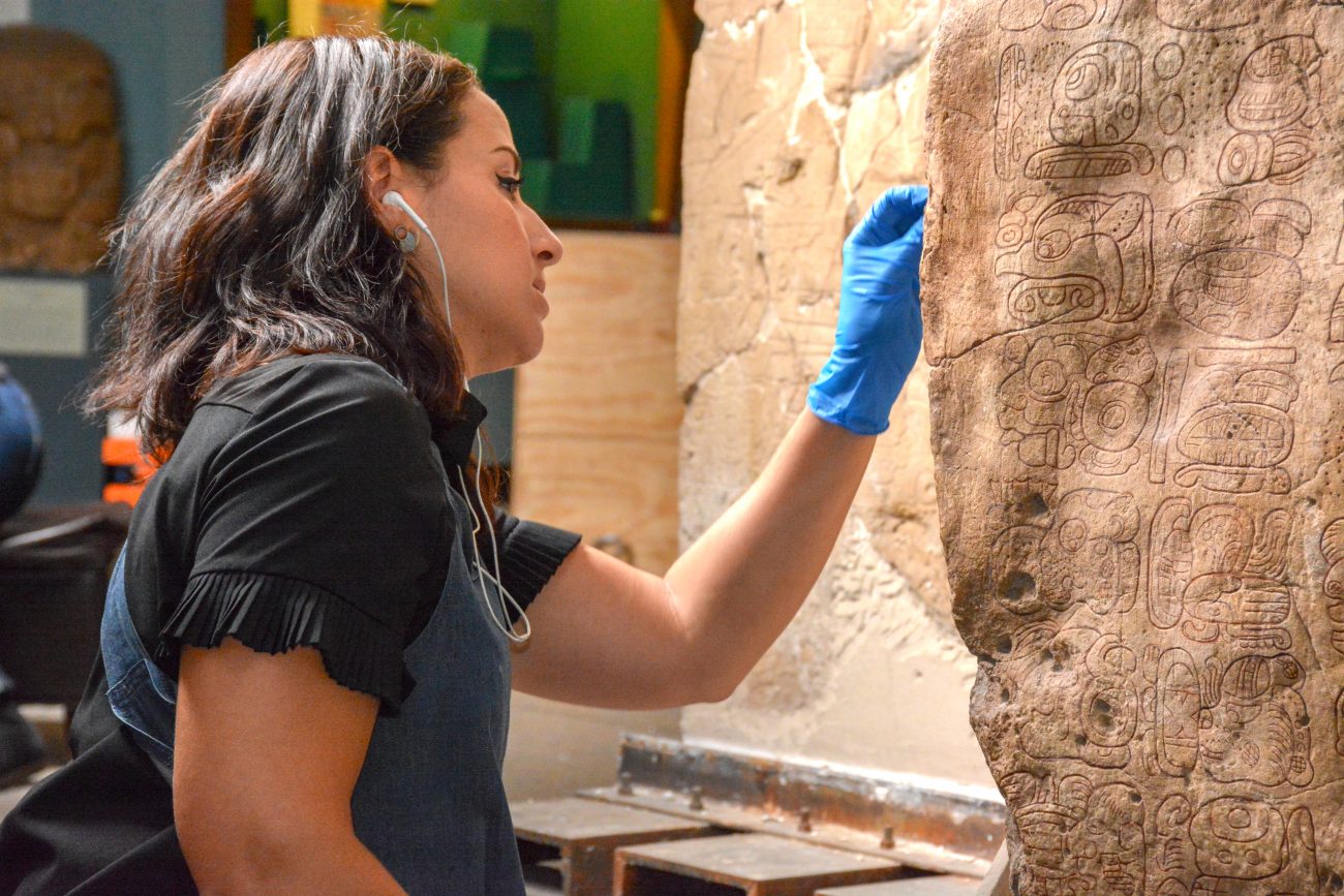 Alexis North, Williams Project Conservator at the Penn Museum, carefully cleans the surface of a monumental Maya artifact, helping to illuminate the intricate glyph writing on its surface.