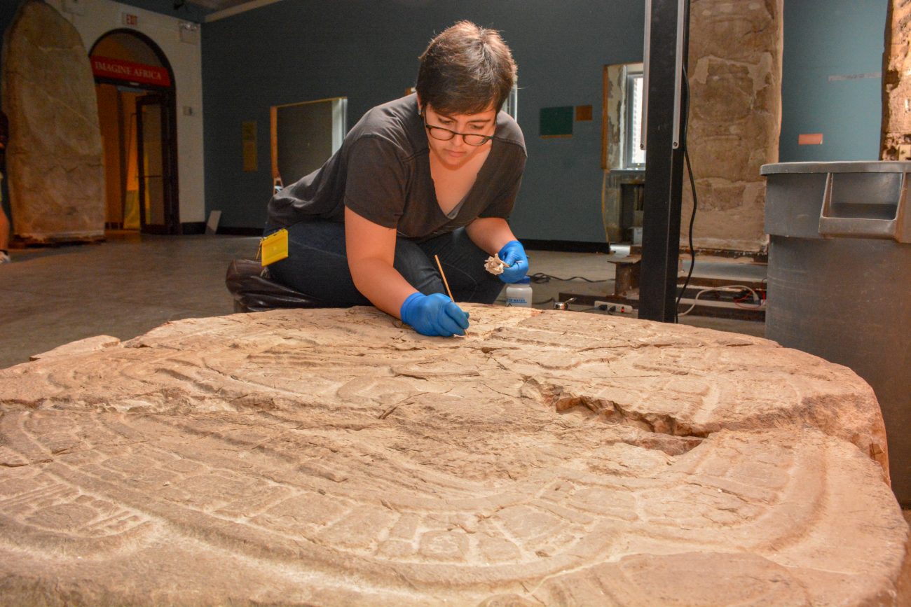 Conservation intern Kate Aguirre works meticulously to remove dirt from a stone altar from present-day Belize, dating to 830 CE.