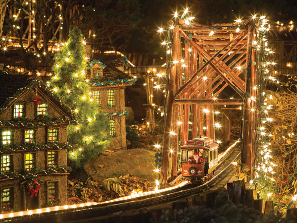 Miniature holiday train crossing a lit bridge in the Holiday Garden Railway at Morris Arboretum.