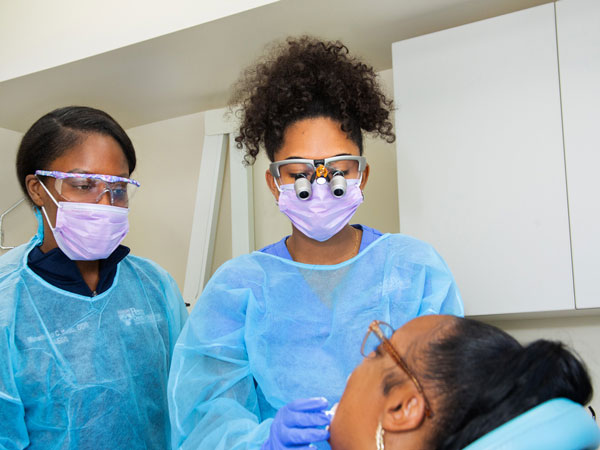 Two dentists in blue scrubs and glasses providing a patient with a dental exam