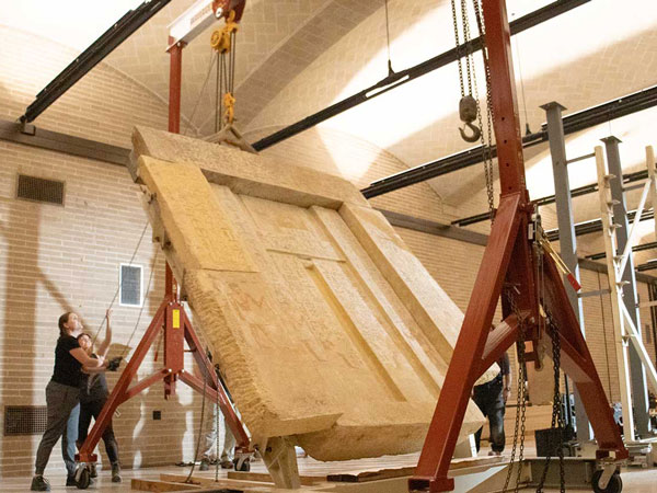 A massive limestone false door from the Tomb Chapel of Kaipure is lifted by a support rig inside the Penn Museum.