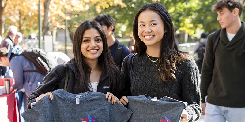 Two Penn students smile while holding up t-shirts, representing the everyday support made possible by the Access and Retention Fund.