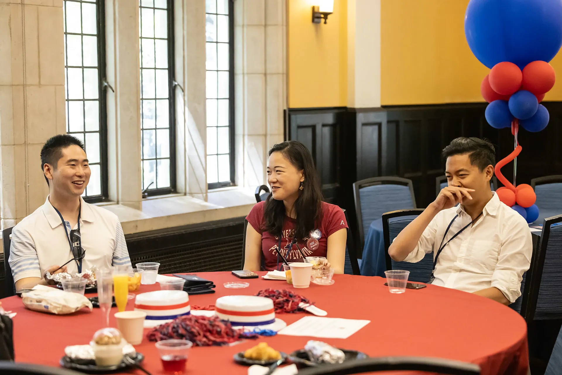 Alumni Weekend attendees enjoy coffee, pastries, and conversation while seated at a festively decorated red table indoors.