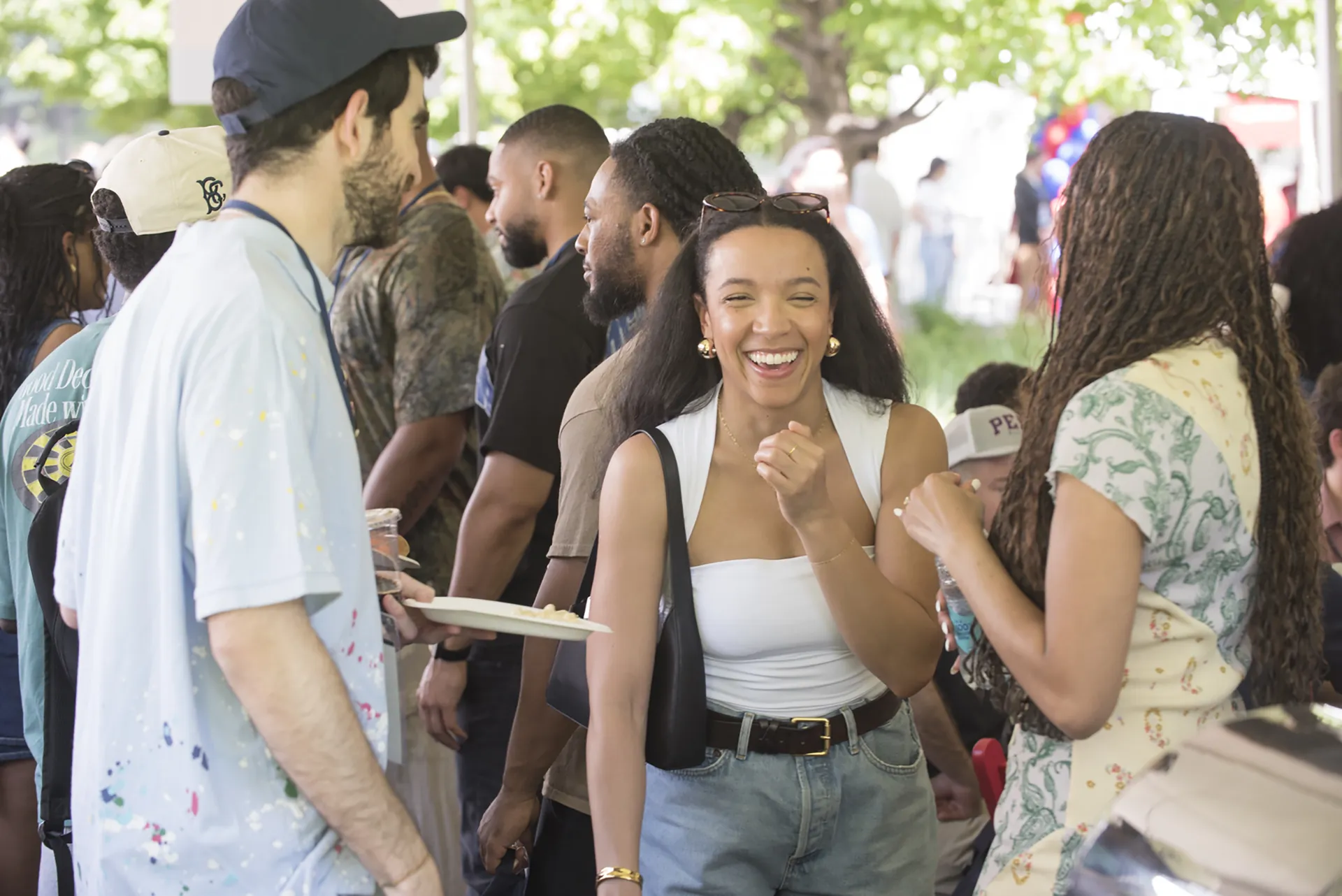 Candid moment of a young Penn alumna laughing and socializing under a canopy with fellow attendees.