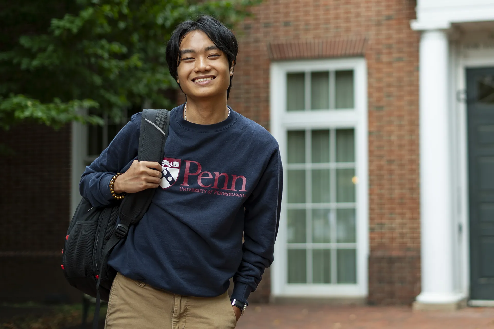 Andrew Luong smiling while standing outside a University of Pennsylvania building, wearing a Penn sweatshirt.