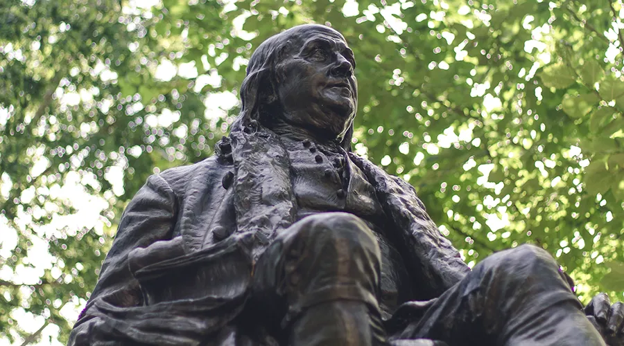 Uplooking view of Ben Franklin statue on Penn campus, framed by greenery.