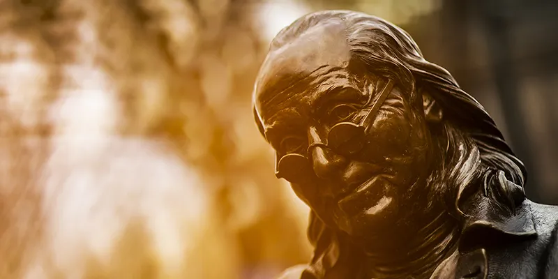 Close-up of the Benjamin Franklin statue on Penn's campus, bathed in golden light.