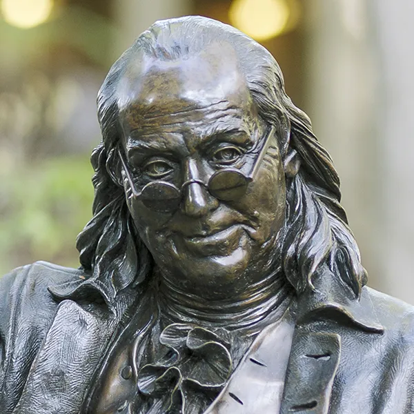 Bronze statue of Benjamin Franklin with glasses perched on his nose, a symbol of Penn’s legacy and intellectual spirit.