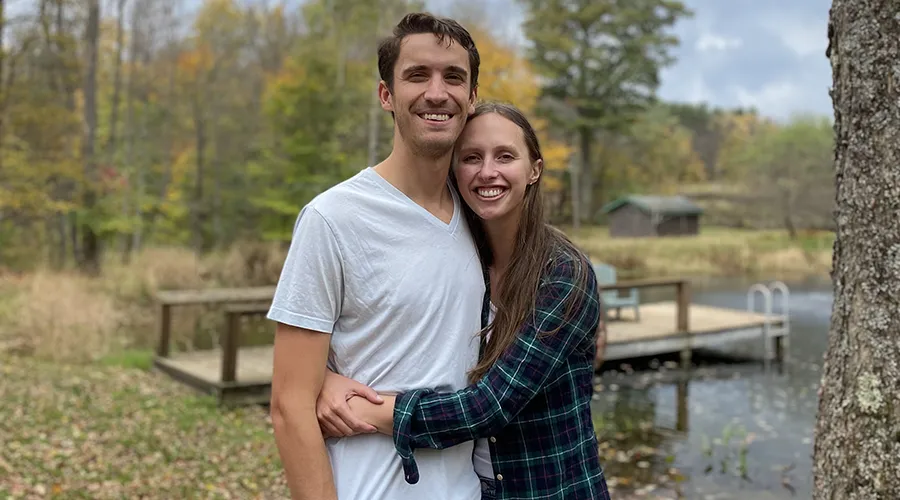 Carly Crist Hutchison and Kent Hutchison standing together outdoors near a pond in autumn
