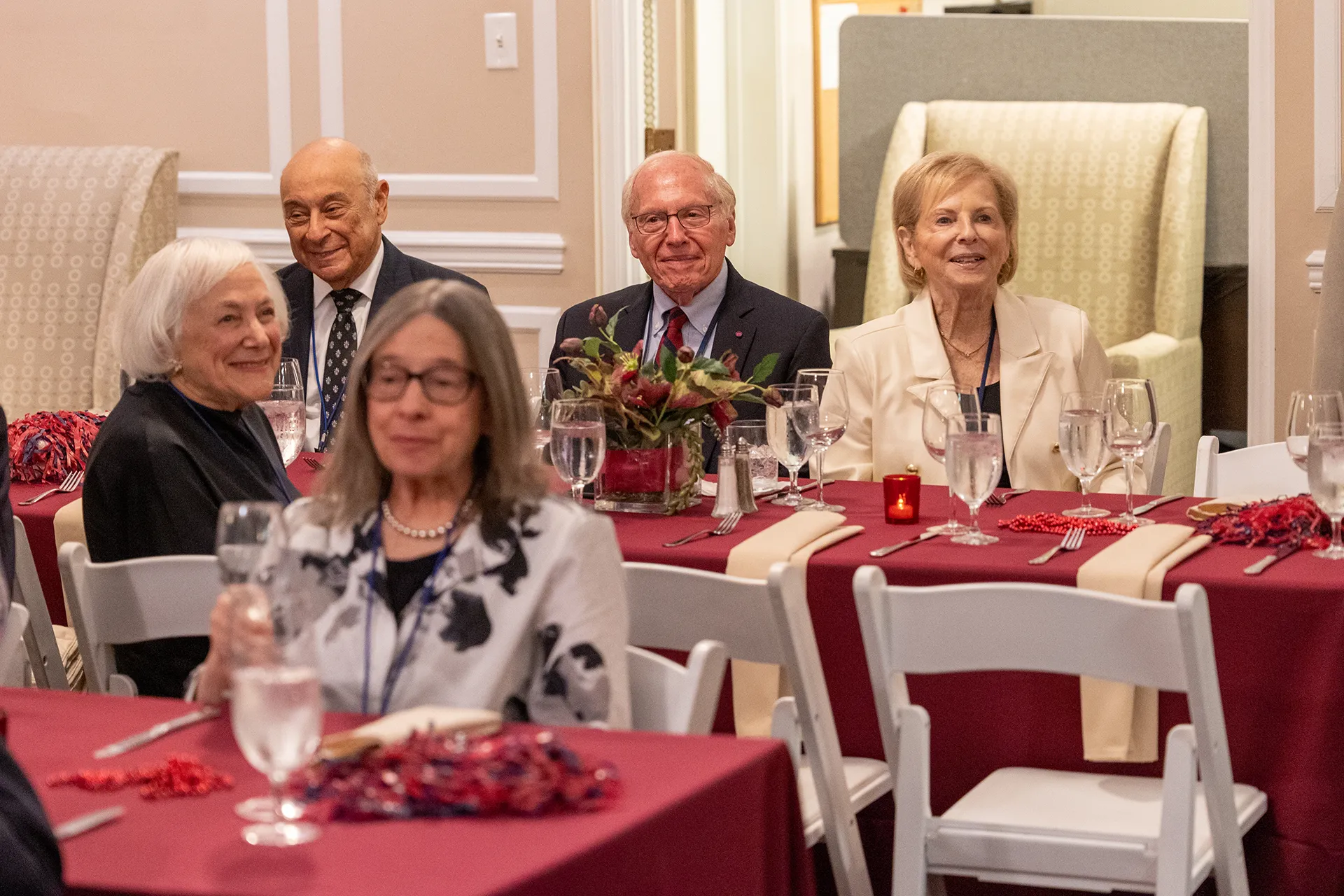 Seated University of Pennsylvania Class of 1960 alumni smiling at their 65th reunion banquet, with burgundy tablecloths and floral centerpieces