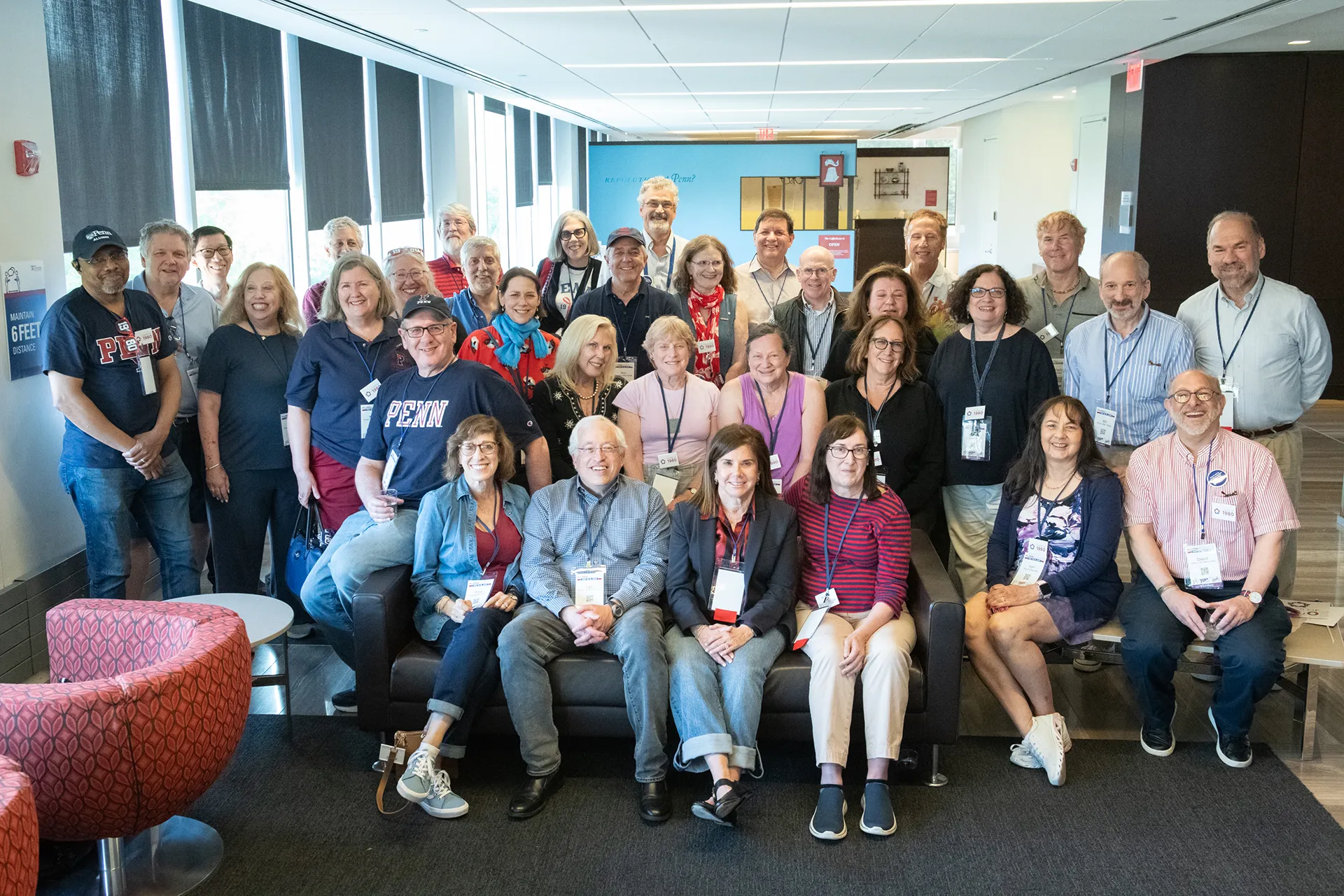 A large group of University of Pennsylvania alumni from the Class of 1980 posing in a modern lounge with floor-to-ceiling windows at their 45th reunion