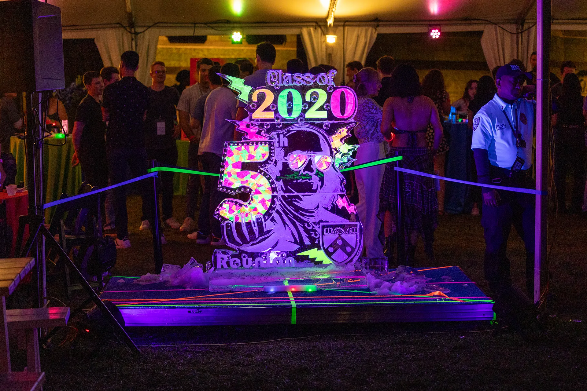 Neon-lit ice sculpture carved with “Class of 2020 5th Reunion” glowing under UV lights at an Alumni Weekend reunion event