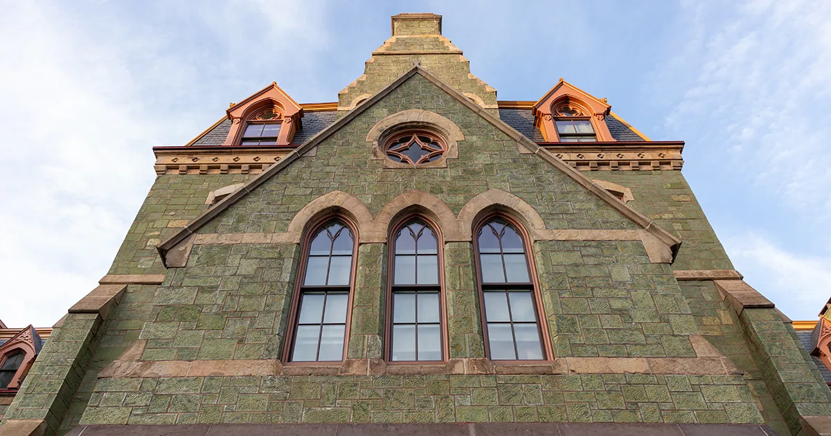 An exterior view of College Hall at the University of Pennsylvania, showcasing the historic building's green stone facade and Gothic-style architecture.