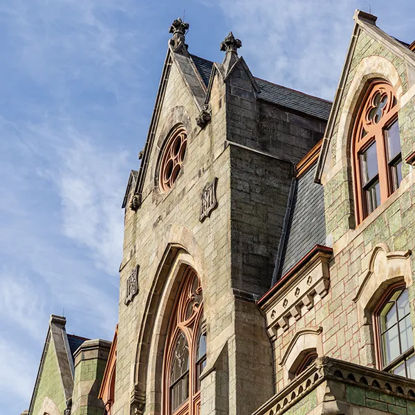 College Hall at the University of Pennsylvania, showcasing its distinctive green stone facade and ornate windows against a bright blue sky.