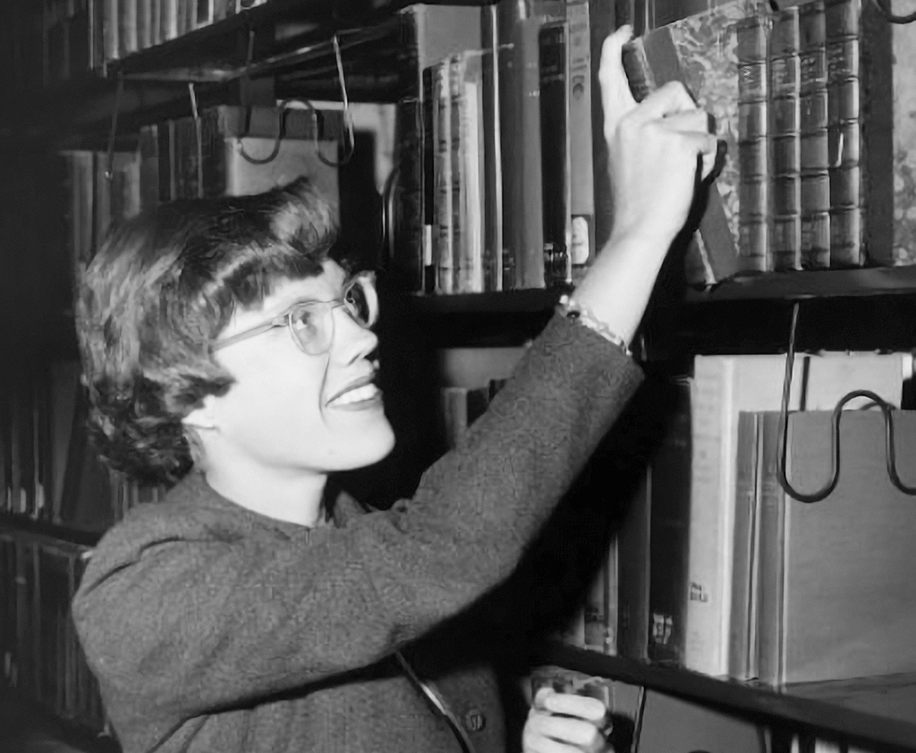 Elizabeth A.R. Brown reaching for a book on a library shelf during her early academic career.