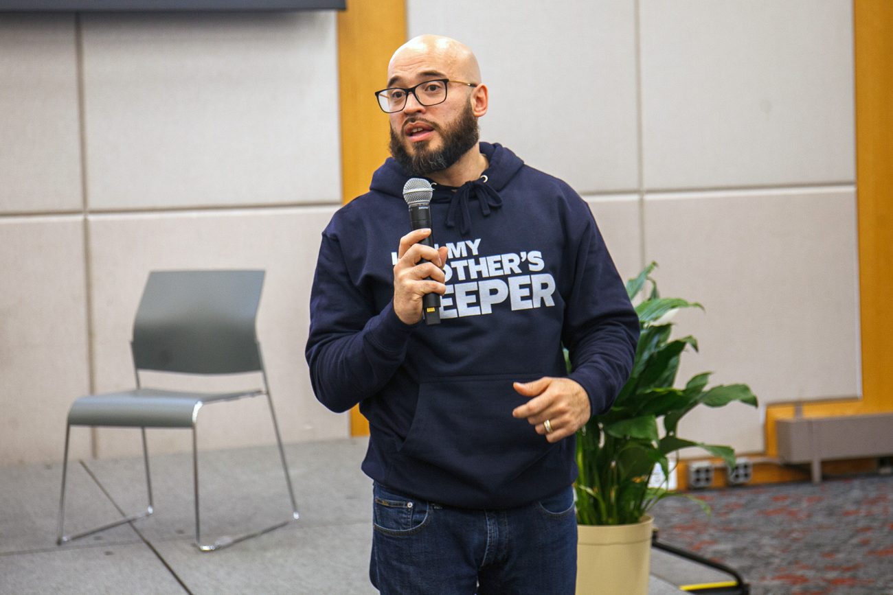 Mark Comesañas, GrEd’26, speaks into a microphone while wearing a "My Brother's Keeper" sweatshirt