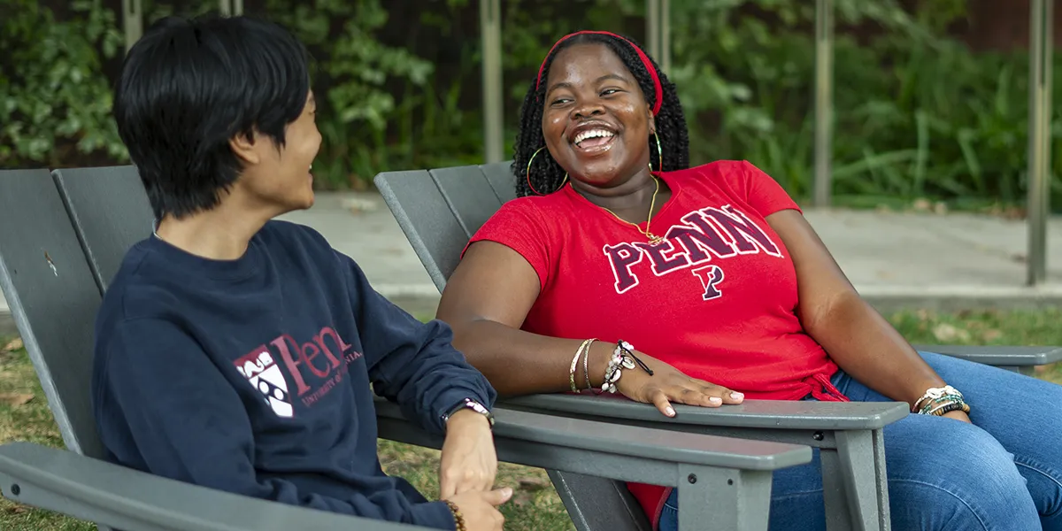 Herinah Asaah smiling and talking with a fellow Penn student outdoors