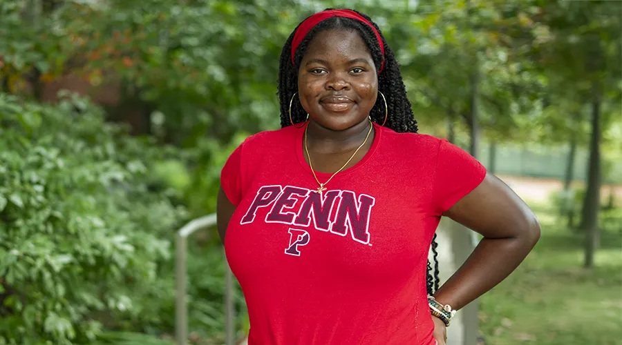Herinah Asaah, C’26, standing outdoors in a red Penn shirt