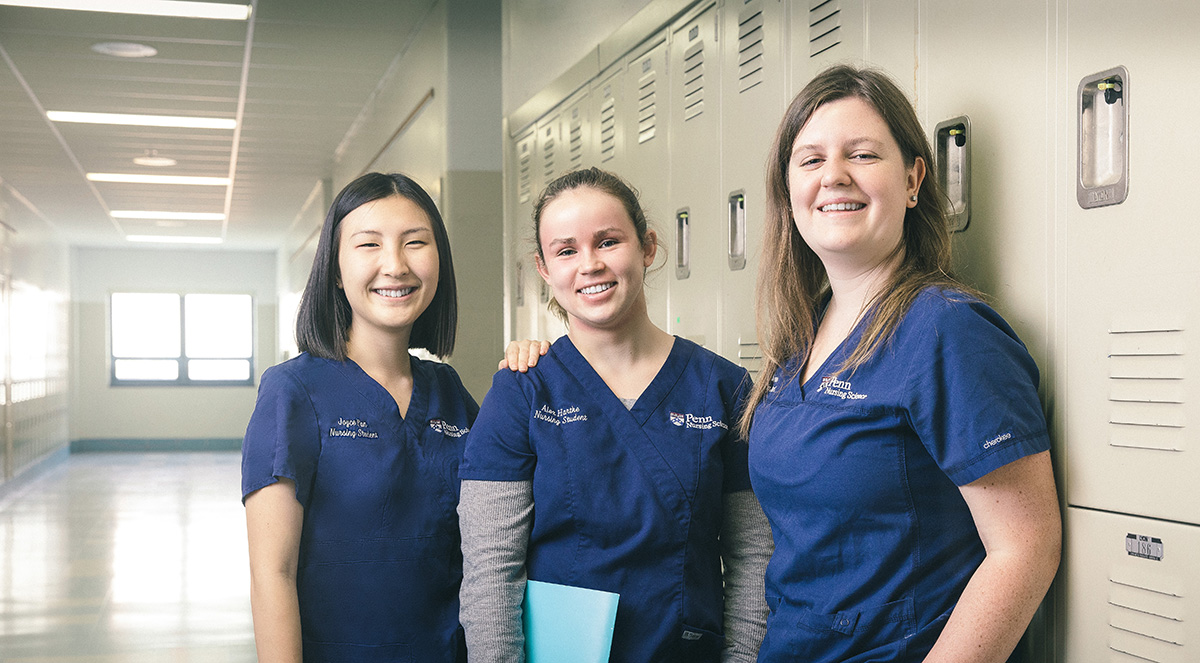 Three Penn Nursing students pose together and smile next to a row of lockers.