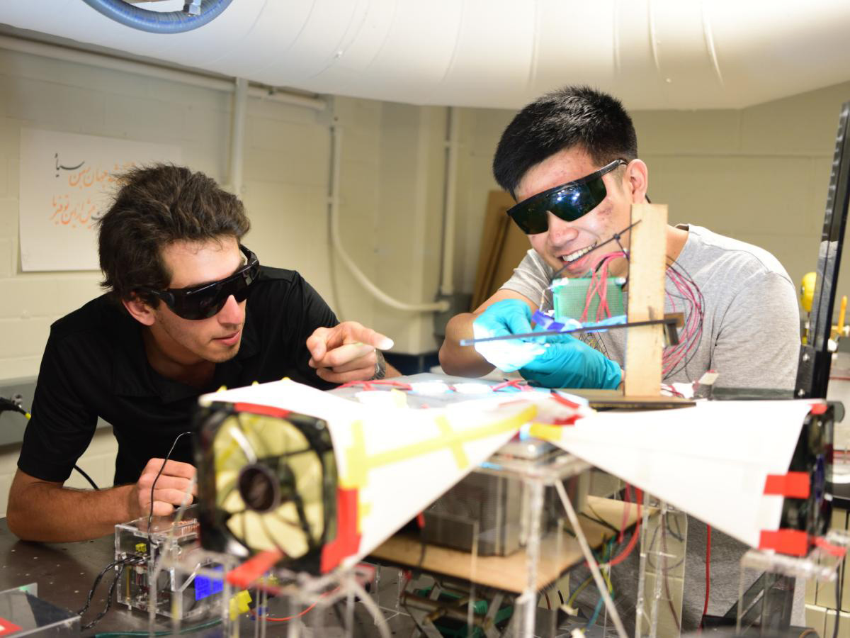 Two students wearing protective glasses work together on an electrical project in a lab.