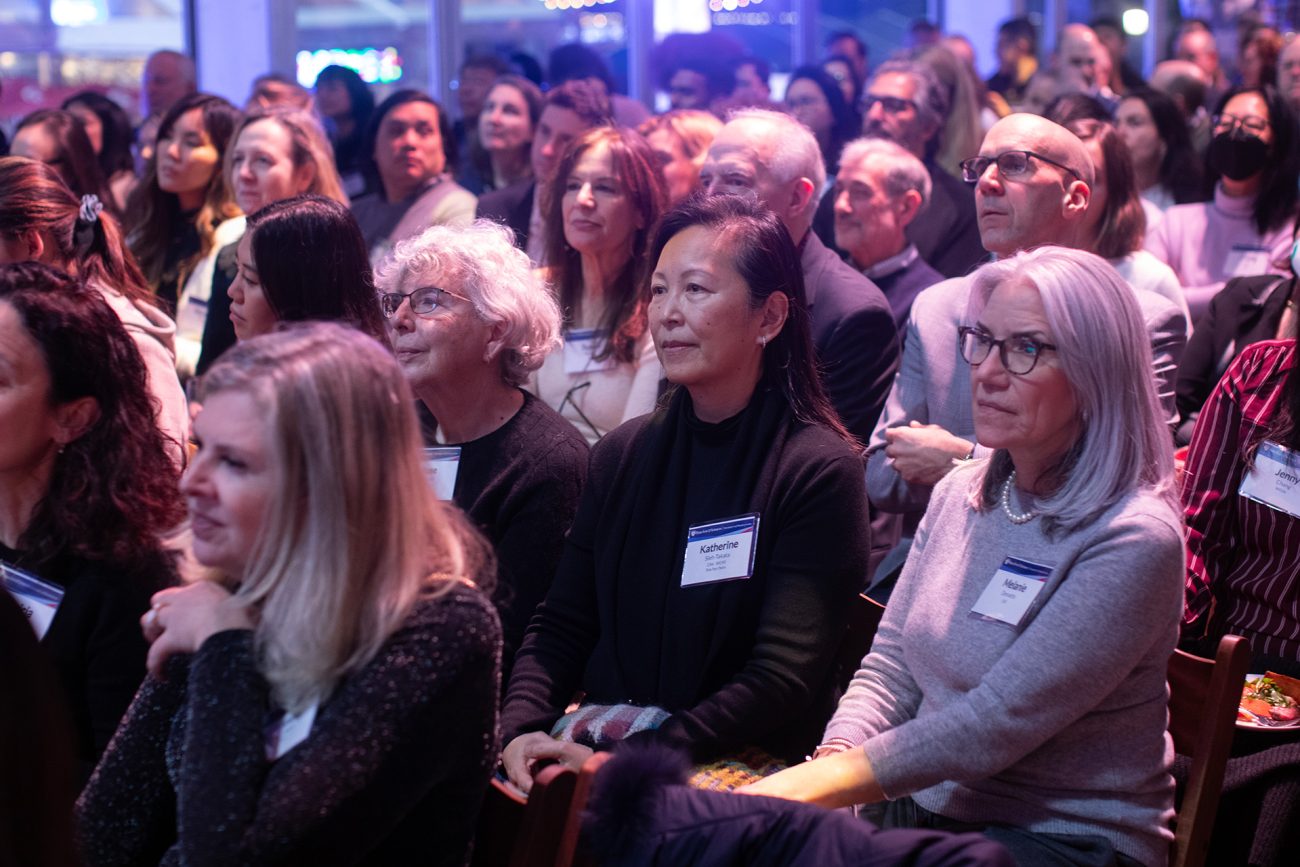 A diverse audience of adults attentively watches an event, showcasing a mix of expressions of interest and contemplation.