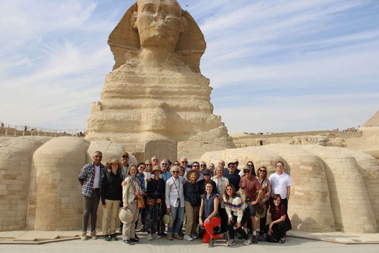 A diverse group of Penn alumni posing for a photo in front of the Great Sphinx of Giza under a clear blue sky.
