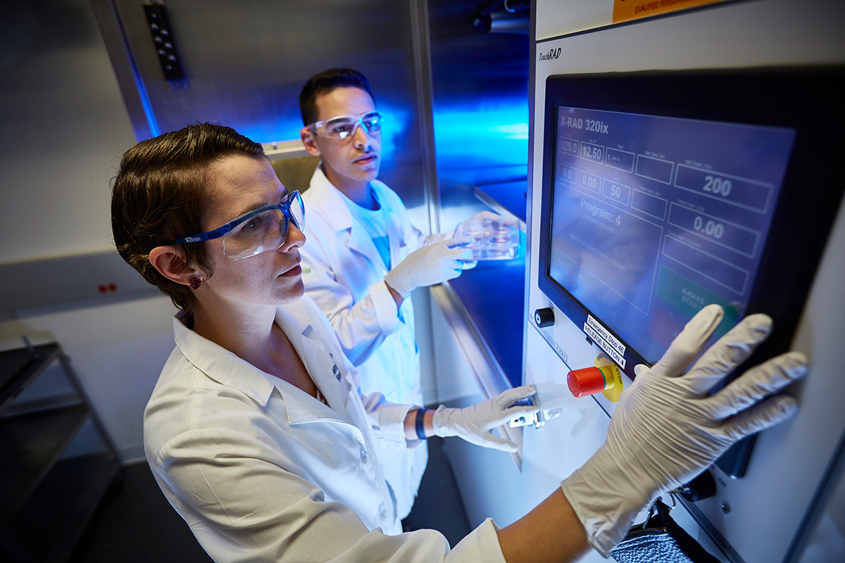 Two laboratory researchers are focused on a procedure involving an advanced X-RAD 320ix machine, shown on the digital display.