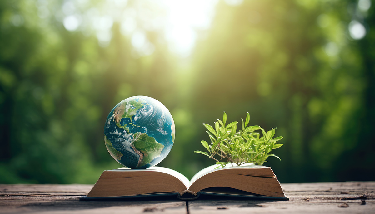A symbolic image depicting environmental education. A small globe rests on an open book with North America visible, positioned on a wooden surface outdoors. Next to the globe, a small, leafy green plant grows from the pages of the book, symbolizing the growth of knowledge about global ecology.
