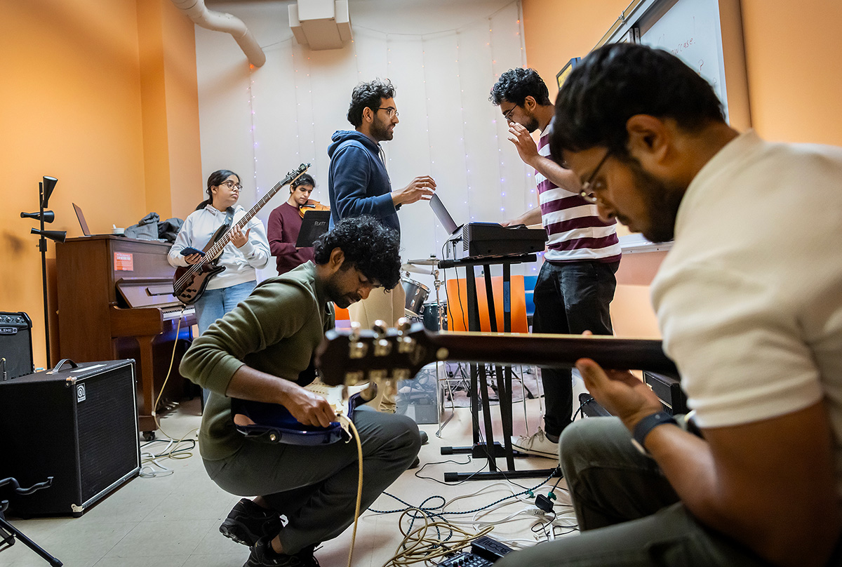 A diverse group of musicians engaged in a spirited jam session in a cozy, warmly-lit room decorated with string lights.