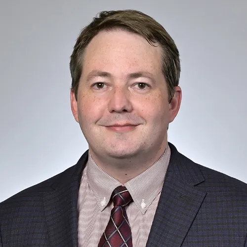 Portrait of Dr. Jonathan Miner, RVCL research expert at Penn Medicine, wearing a dark checked blazer and red patterned tie.