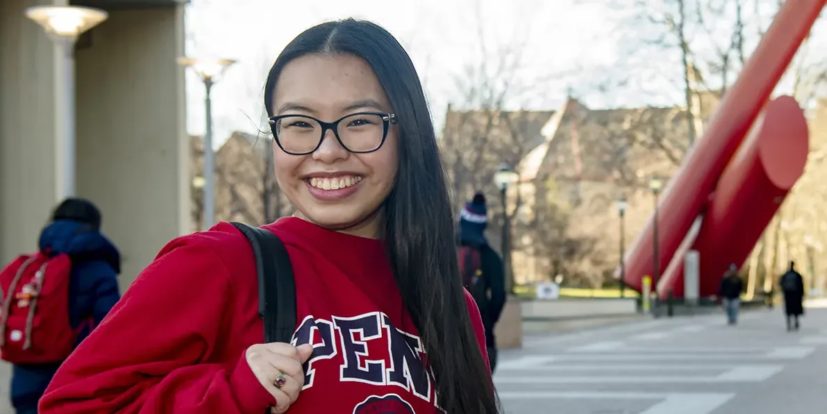 Kristina Pham smiles with a Penn sweatshirt and backpack near the Covenant sculpture