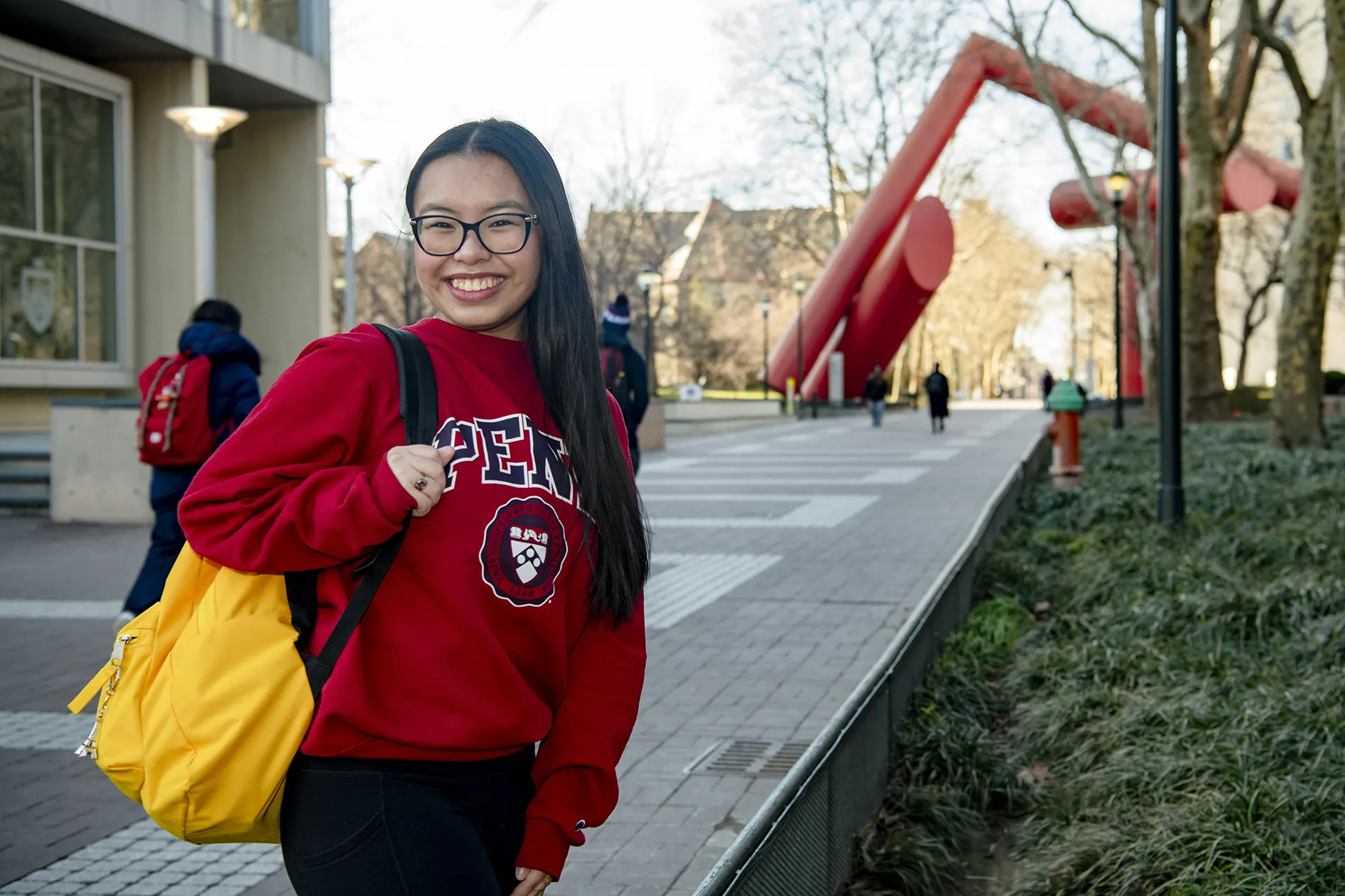 Kristina Pham smiling in front of the Covenant sculpture, carrying a yellow backpack at Penn