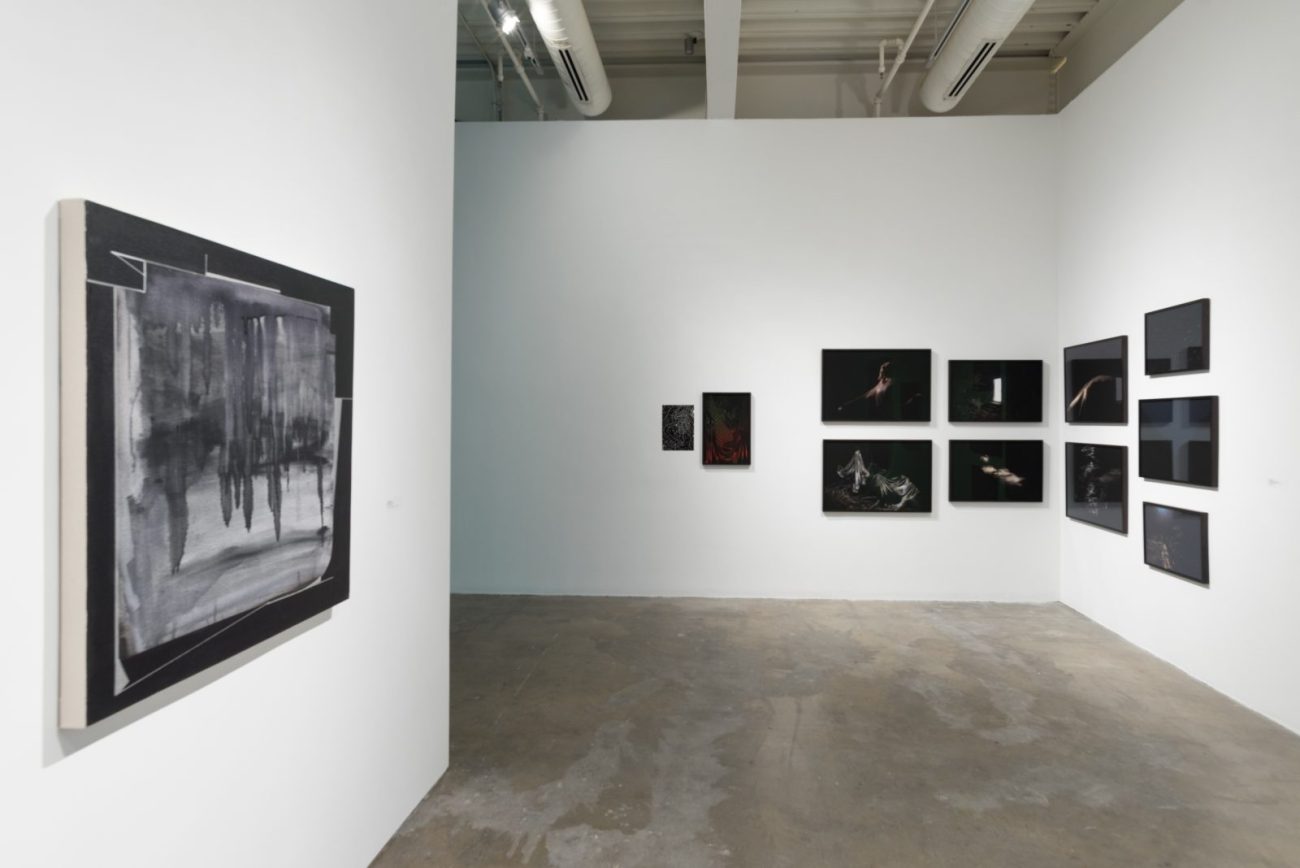 A black-and-white painting on the left wall, showing forms without clear shape, complements a group of screens on the rear and right walls showing clear, colored forms on black backgrounds