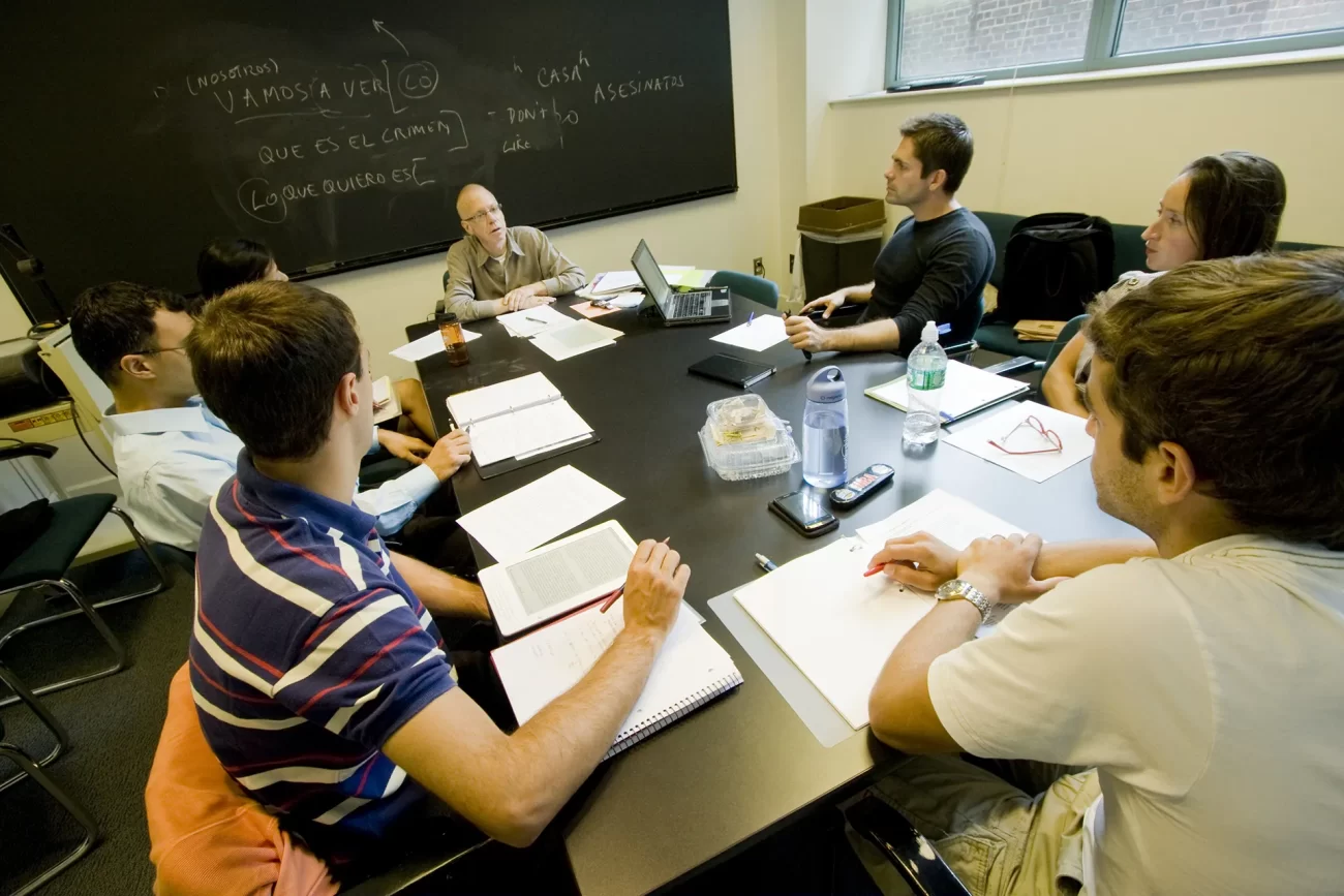 Students seated around a table in a classroom discussing course material with an instructor.