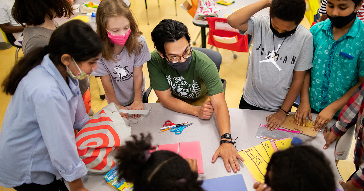 A teacher affiliated with the McGraw Center for Educational Leadership engages in coversation with young students in an elementary school.