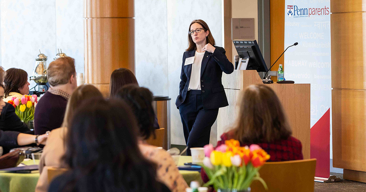 A woman in a suit speaks to the group during a Penn Parents Council meeting