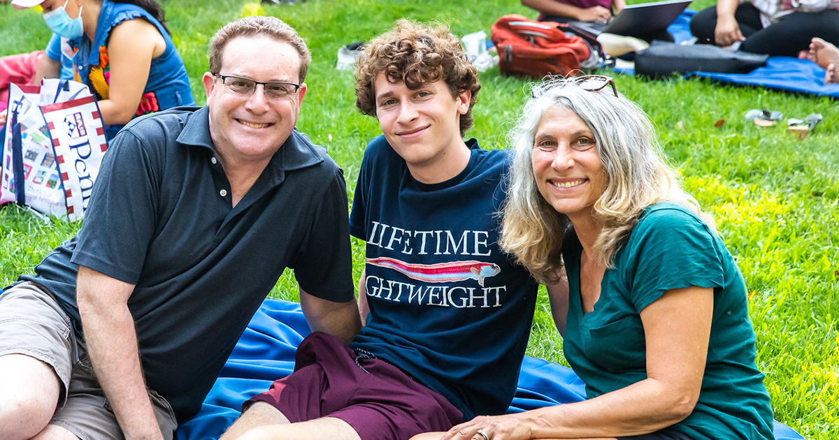 A Penn student sits with his parents on a picnic blanket on College Green